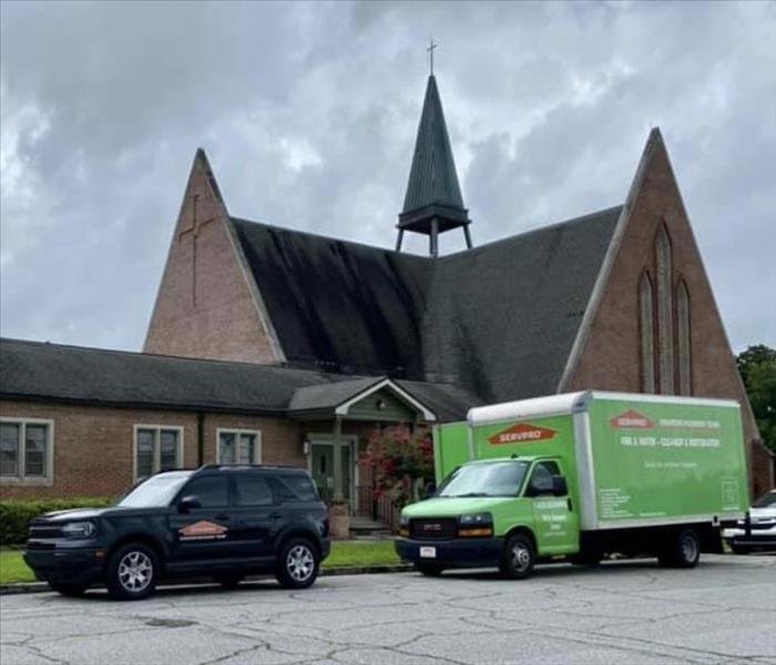 a green and a black SERVPRO truck is shown in front of a church where they are working
