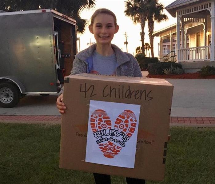 Young girl holds a large box full of shoes that were donated at event.