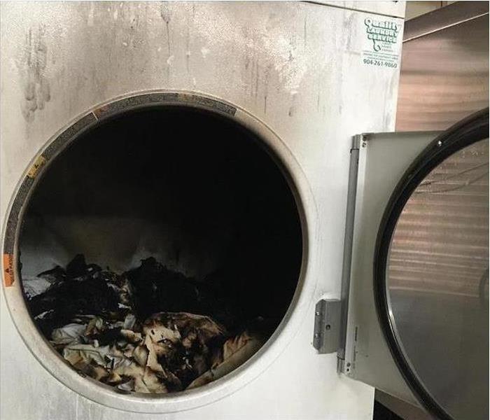 White dryer with the door open and the inside is covered with burnt towels after a fire caught inside the dryer.