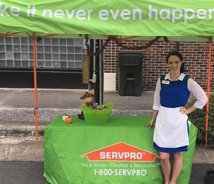 Green SERVPRO tent and table. Girl with brown hair dressed as Belle from Beauty and the Beast in the village blue dress.
