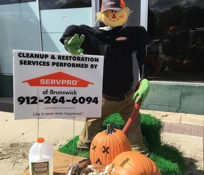 2 orange pumpkins spitting up seeds + SERVPRO scarecrow cleaning up the mess.