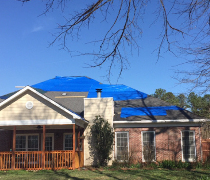 Brick house with blue tarp on roof.